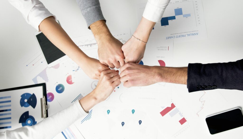 home Colleagues celebrate success with a fist bump over financial charts depicting teamwork and unity.